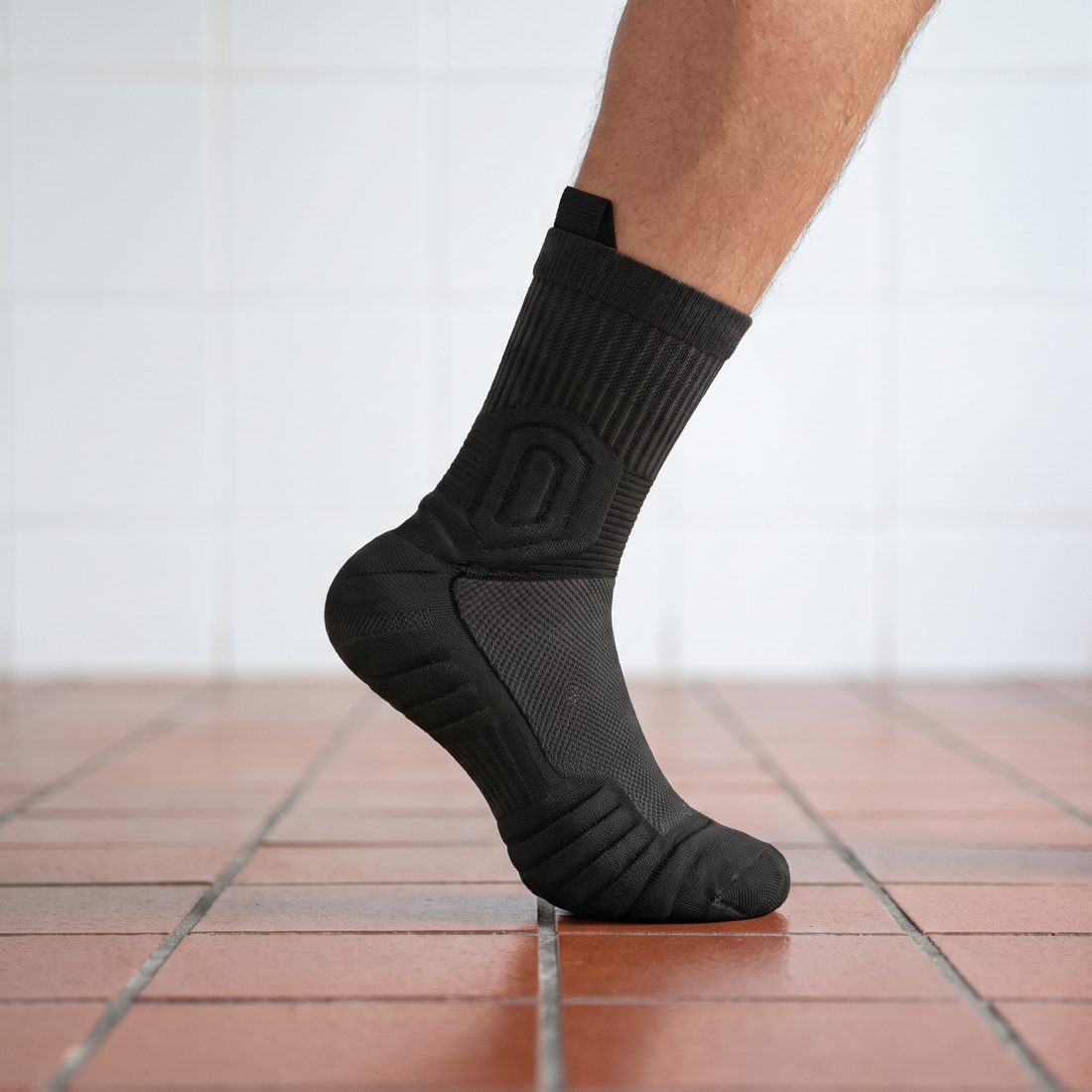 Man's foot on tiptoe in a black Shift Sock on red kitchen floor tiles.