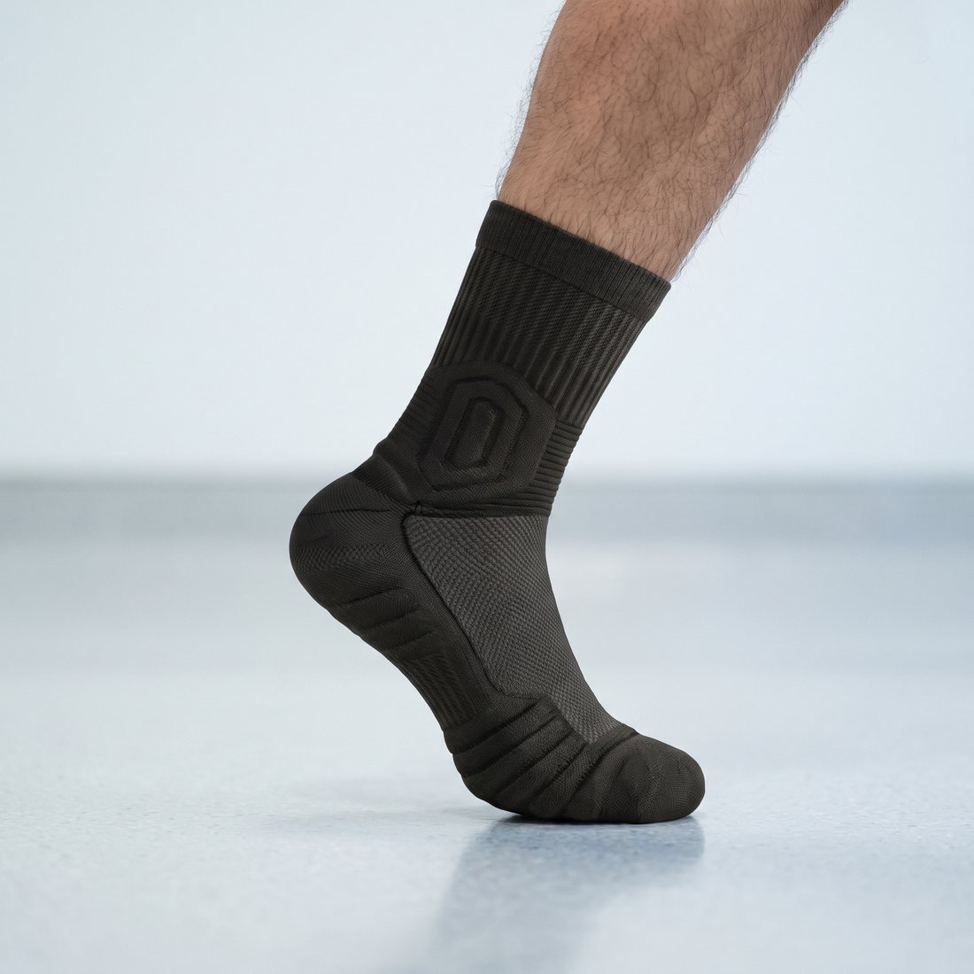 Man's foot on tiptoe in a black Shift Sock on a pale hospital floor.
