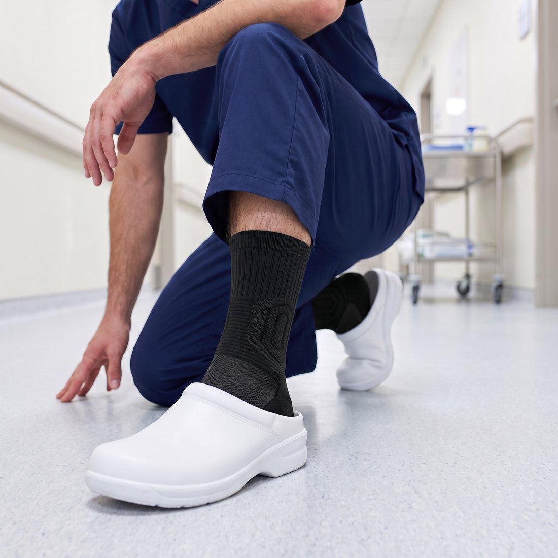 Male nurse crouching in a hospital corridor, black Shift Sock sitting snug above a white clog.