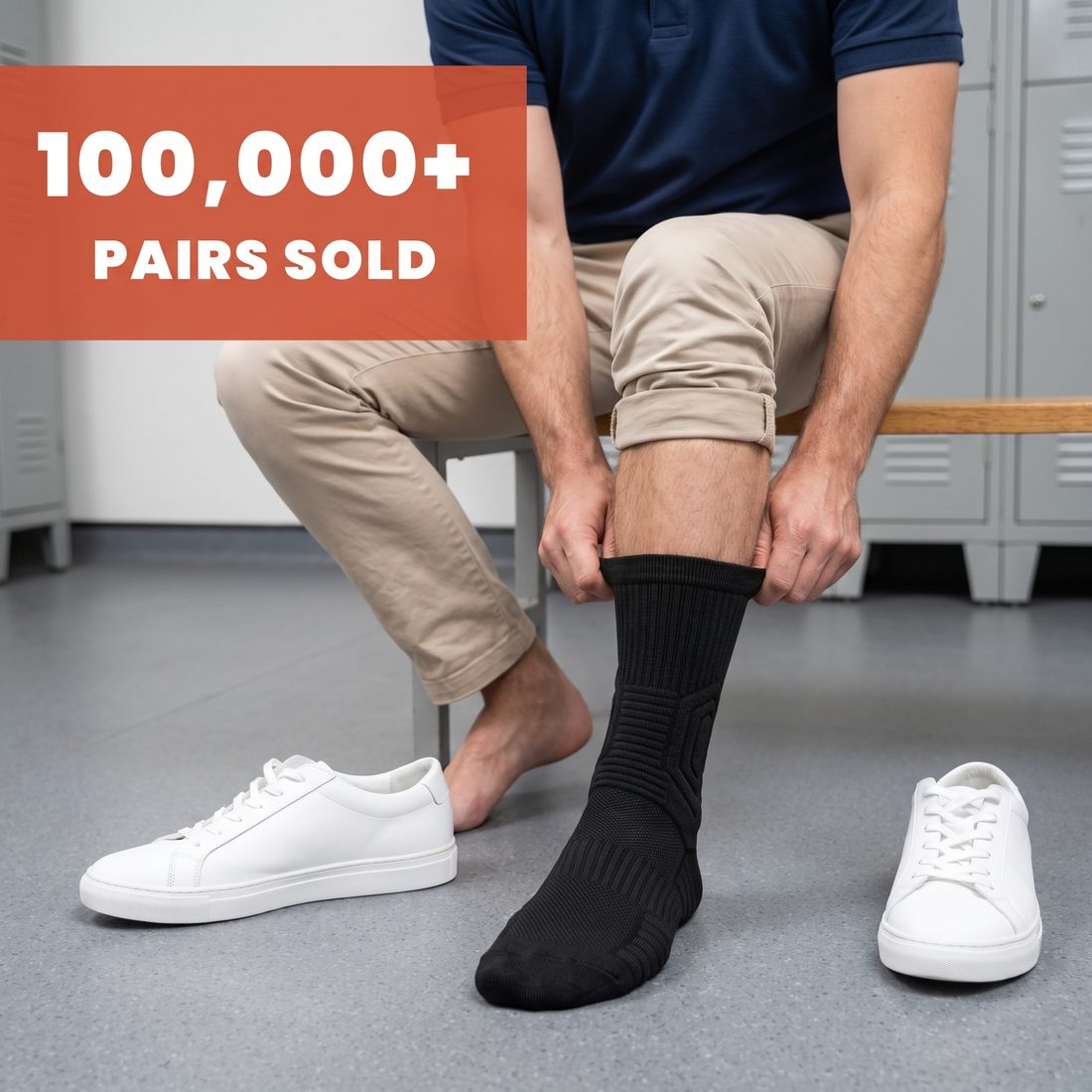 Male retail worker on a locker room bench pulling on a black Shift Sock, white sneakers beside him, 100,000+ pairs sold.