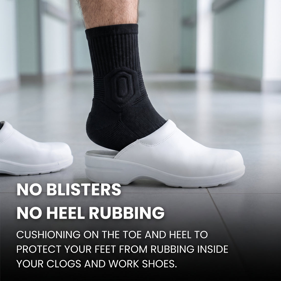 Man's foot in a black Shift Sock sliding into a white hospital clog on a tiled floor.