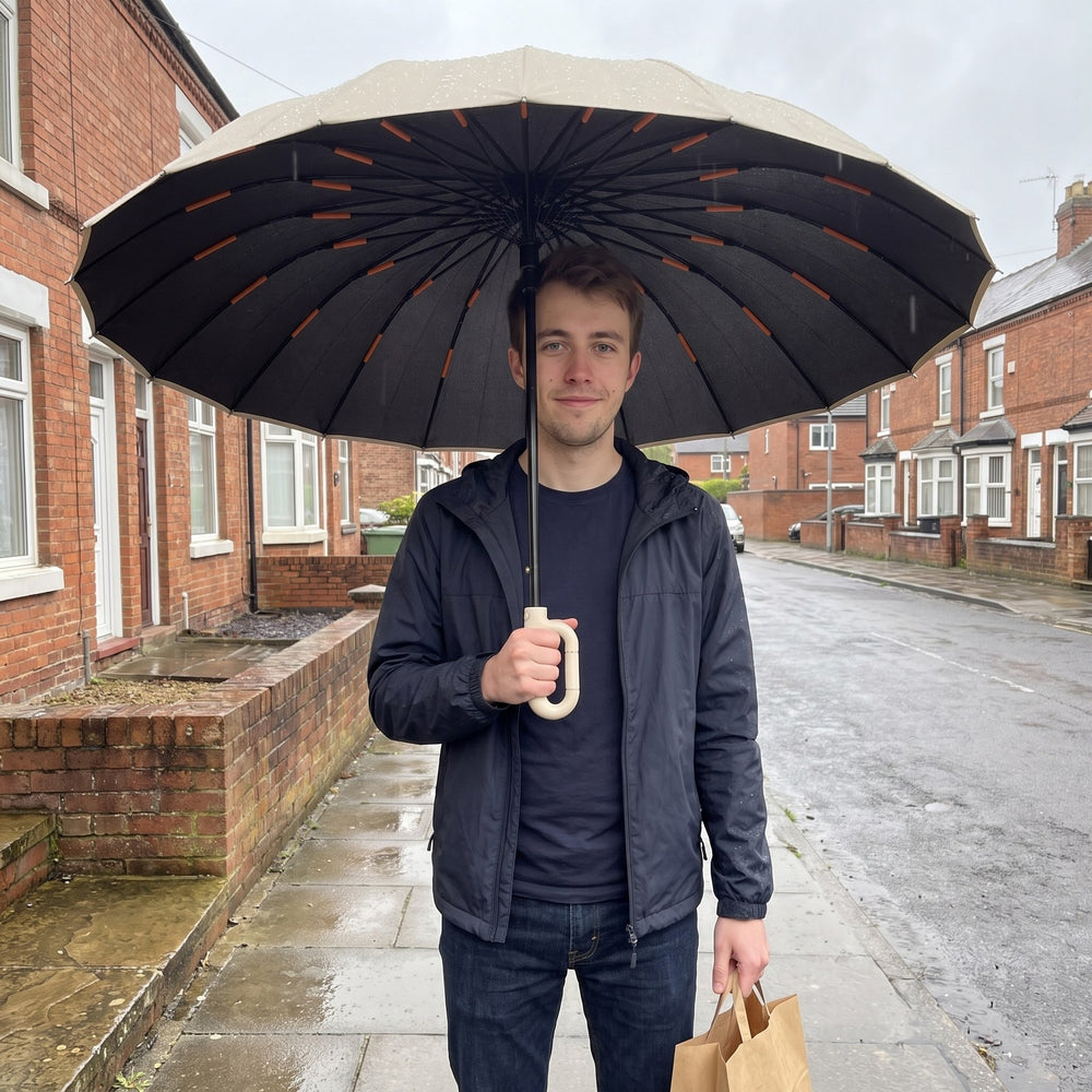 A man standing under an open umbrella on a rainy terraced street, a bag of shopping in his other hand
