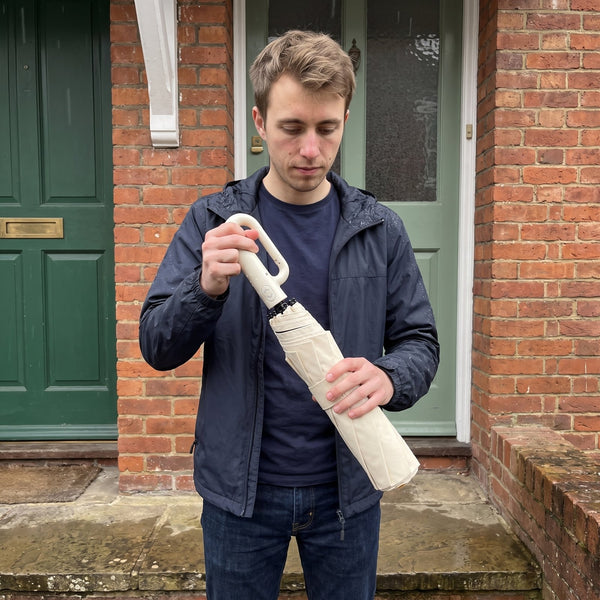 A man at his front door folding a beige umbrella closed
